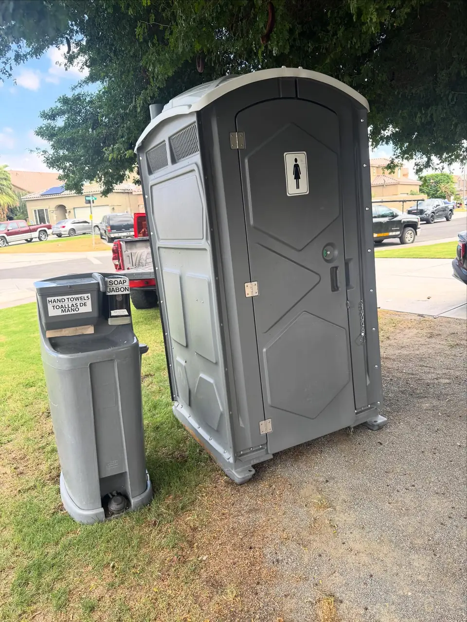 Grey porta potty with a hand washing station on a lawn
