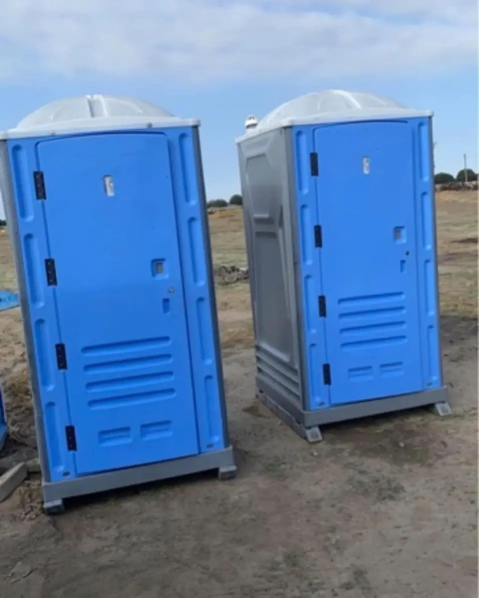 Two blue standard porta potties on a jobsite under a blue sky